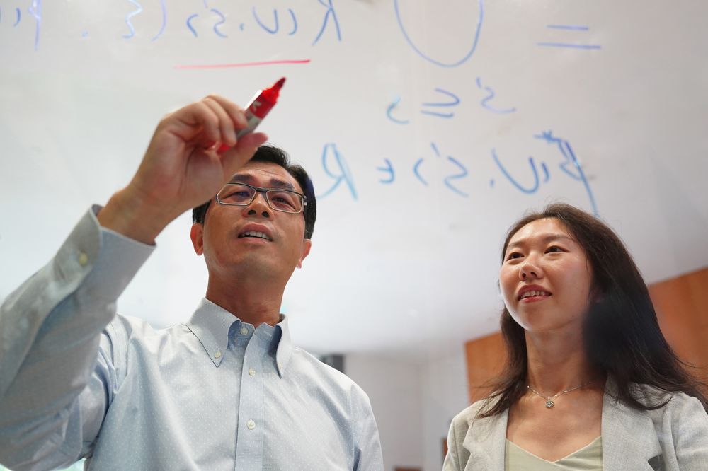 Two people writing the mathematical framework for a fairer AI model on a clear glass wall